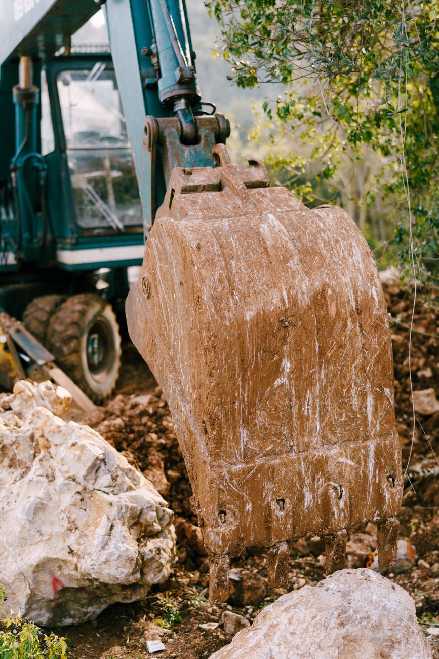 An excavator bucket lifting a large boulder
