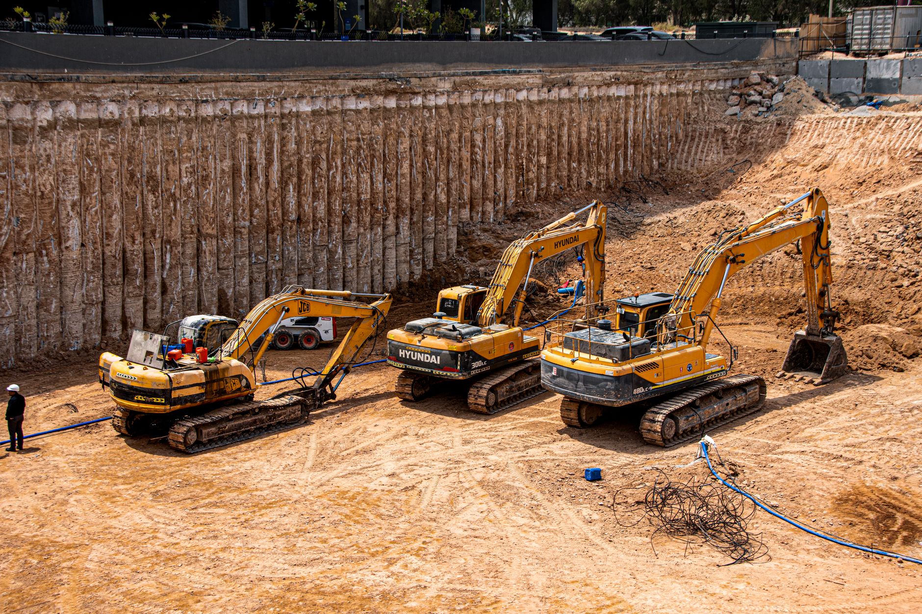 Three excavators standing together at the foot of a shored cut face