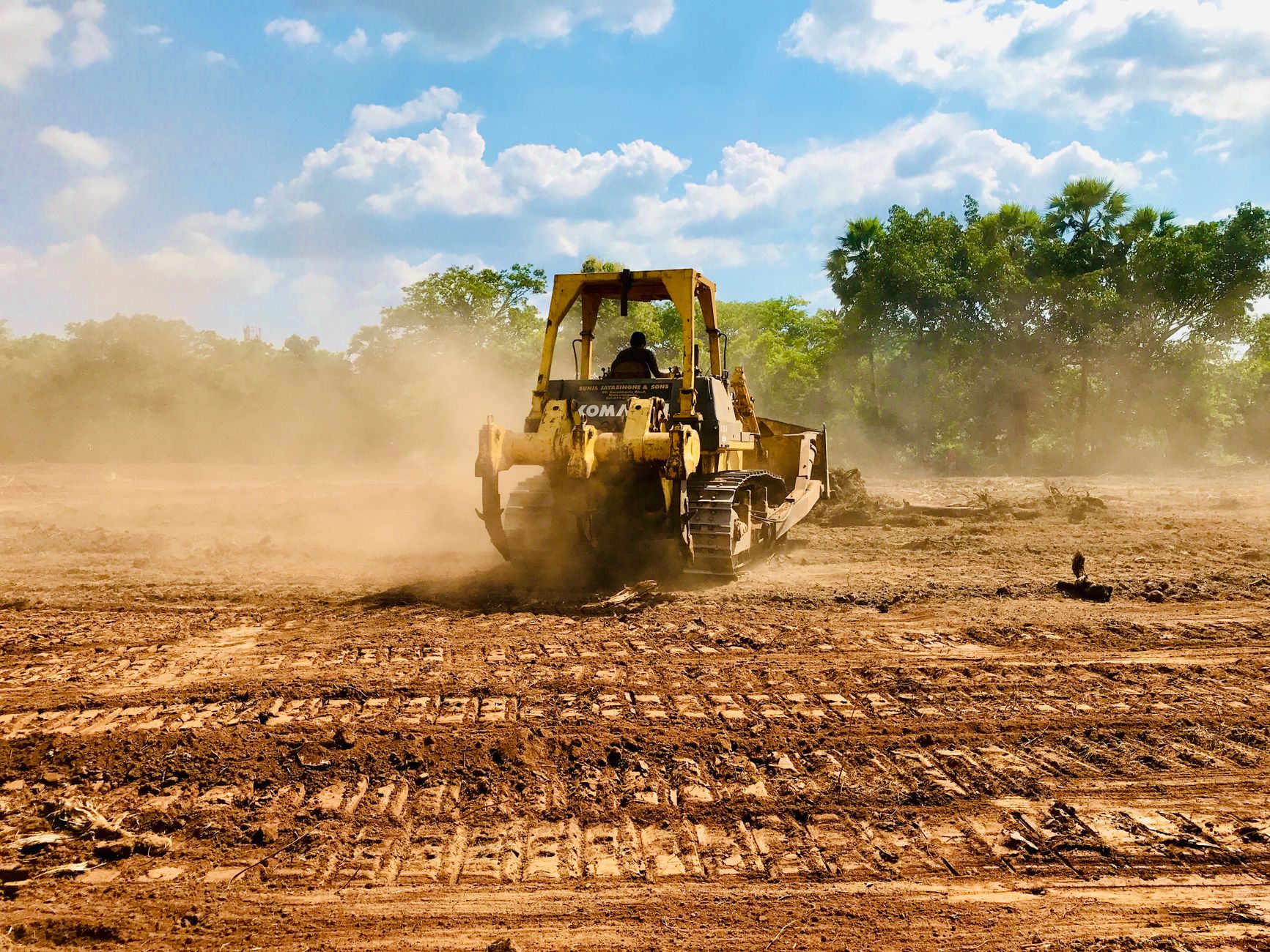 A bulldozer pushing topsoil, raising dust