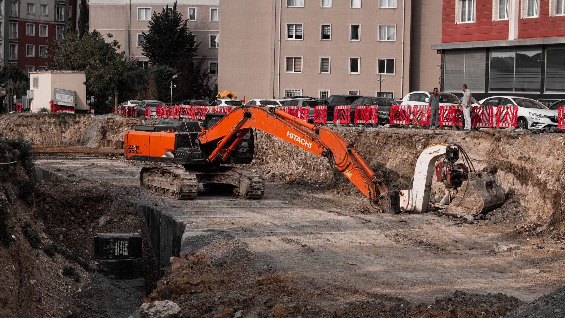 An excavator working at the bottom of a deep excavation between buildings
