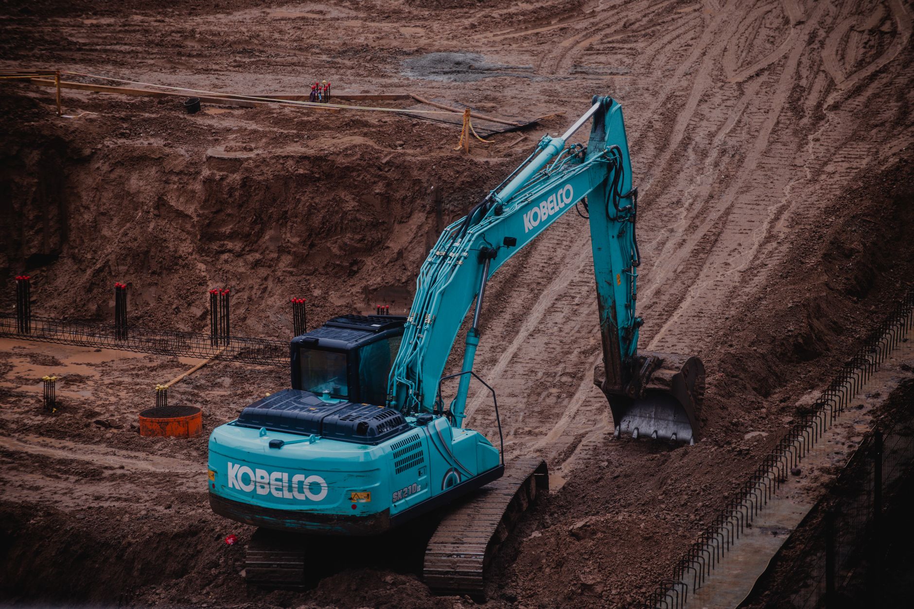 An excavator working at the base of a large cut face of red earth